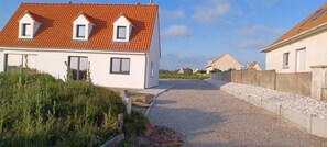 A residential area with a house featuring a red-tiled roof, white exterior walls, and a gravel driveway.