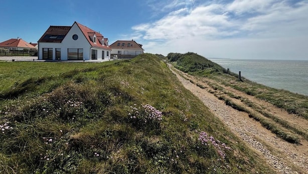 Una propiedad costera con un edificio blanco, un sendero de tierra y vista al mar.