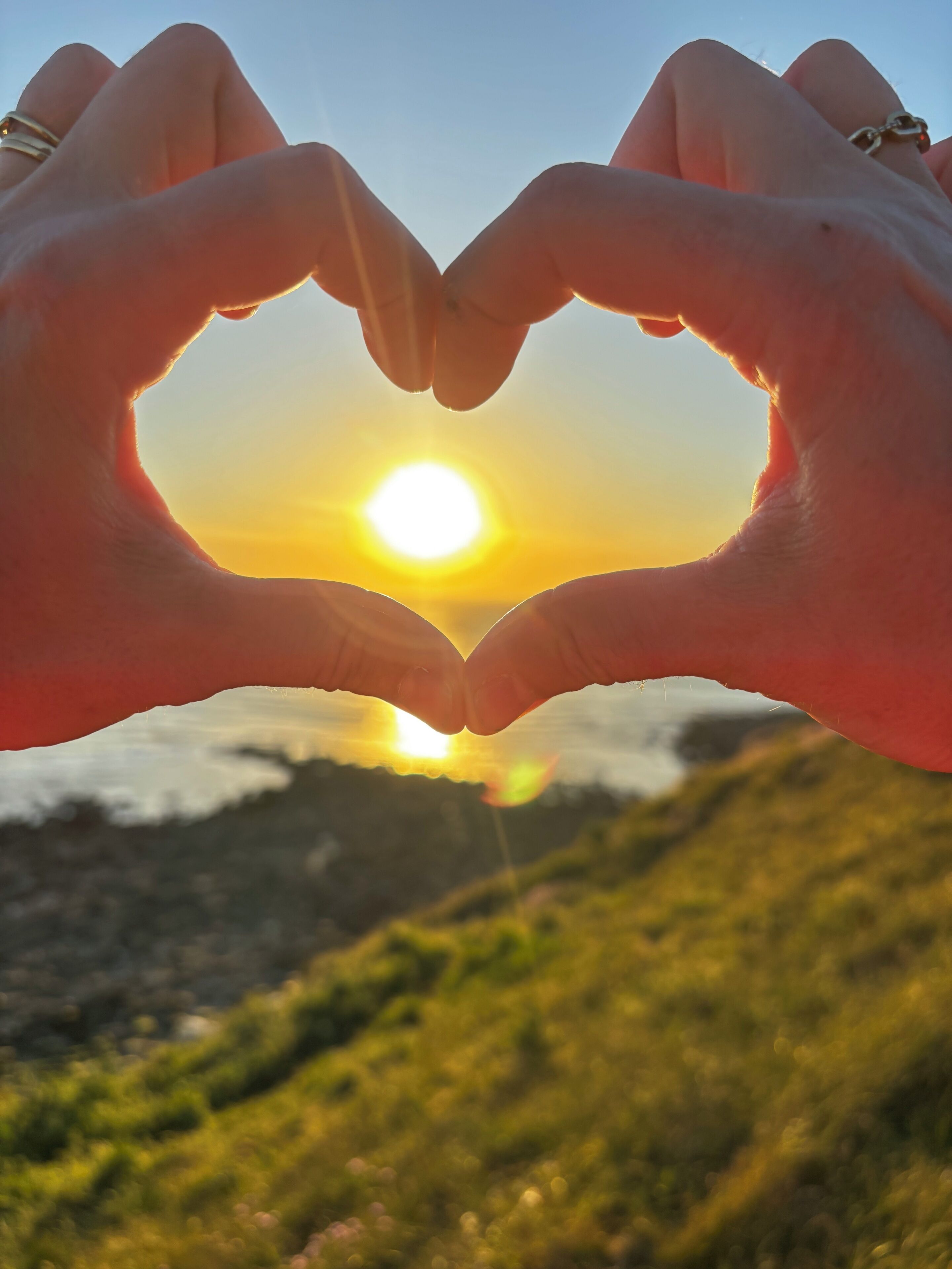 Hands forming a heart shape with the sun in the background.