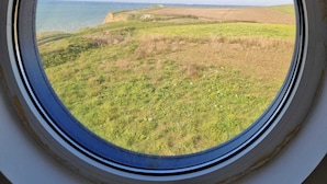 Un ventanal circular con vistas a un campo cubierto de hierba y una costa lejana.