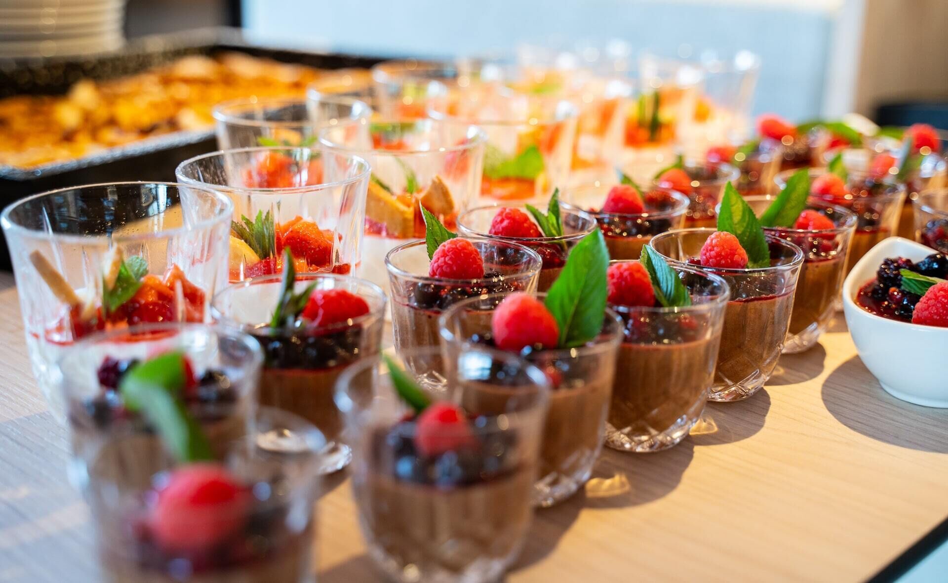A variety of desserts and beverages, including chocolate mousse cups garnished with berries and mint leaves, arranged on a wooden table.