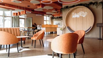 A modern cafe interior with round wooden tables, orange chairs, and a neon sign reading "Legato".