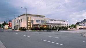 A modern hotel with a covered entrance, a parking lot, and a clear sky. - Hotel Novapart (Wels)