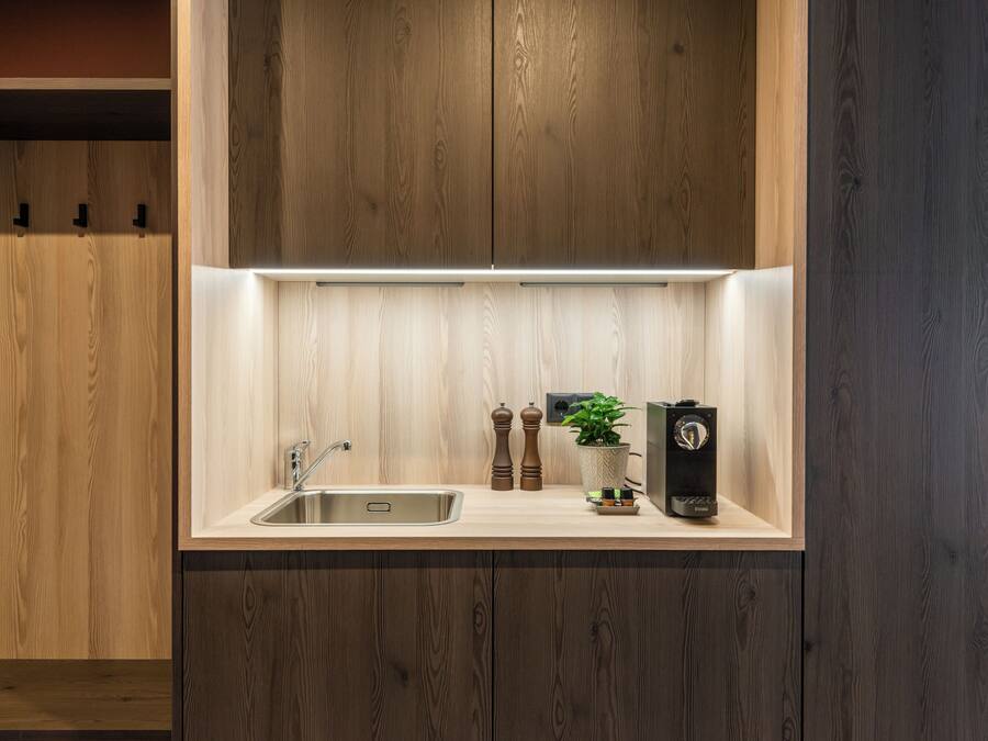A modern kitchen with wooden cabinetry, a stainless steel sink, a coffee machine, and a potted plant.