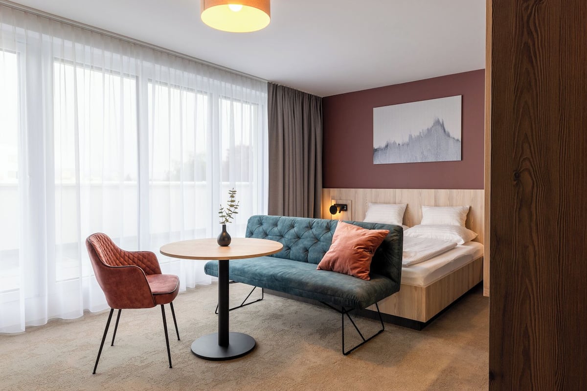 A modern hotel room with a bed, a sofa, a round table, and a chair.