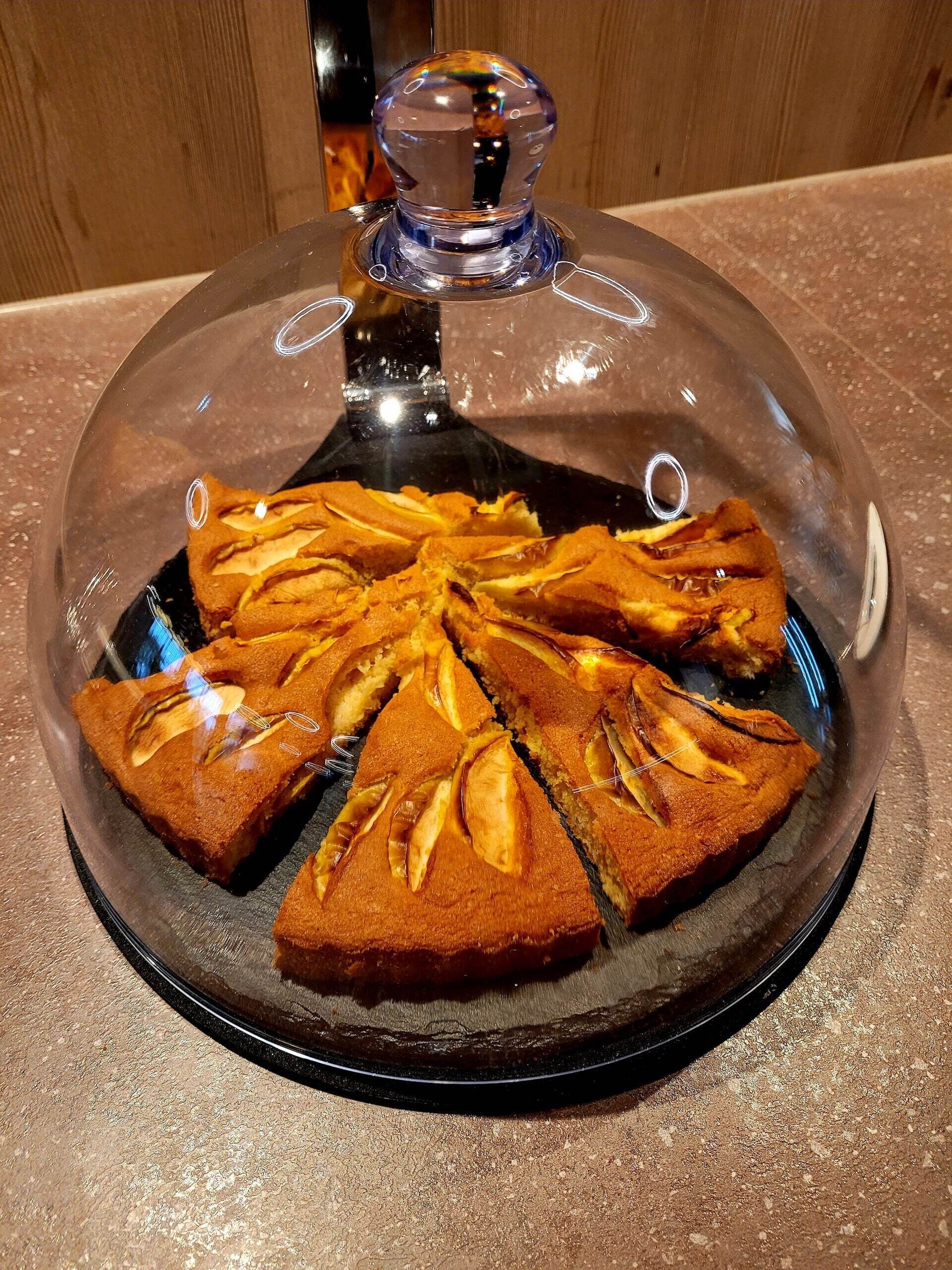 A cake with a glass dome on a black plate.