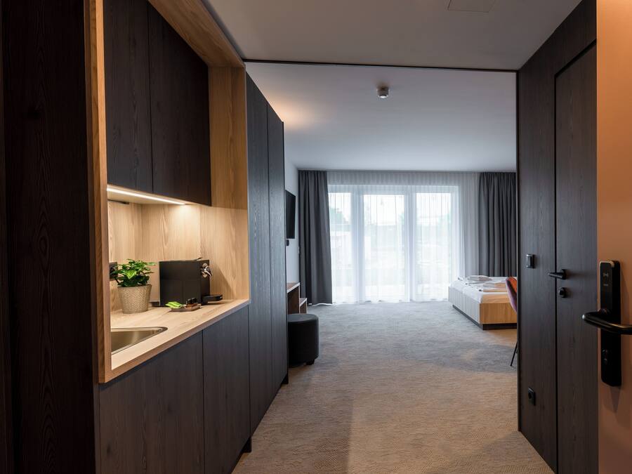 Una habitación de hotel moderna con kitchenette, una cama y un ventanal grande con cortinas.