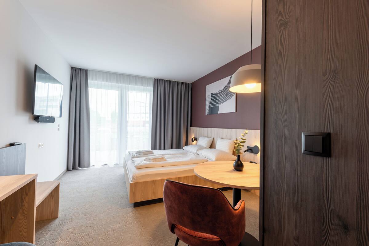 A modern hotel room with a bed, a desk, a chair, a television, and a lamp.