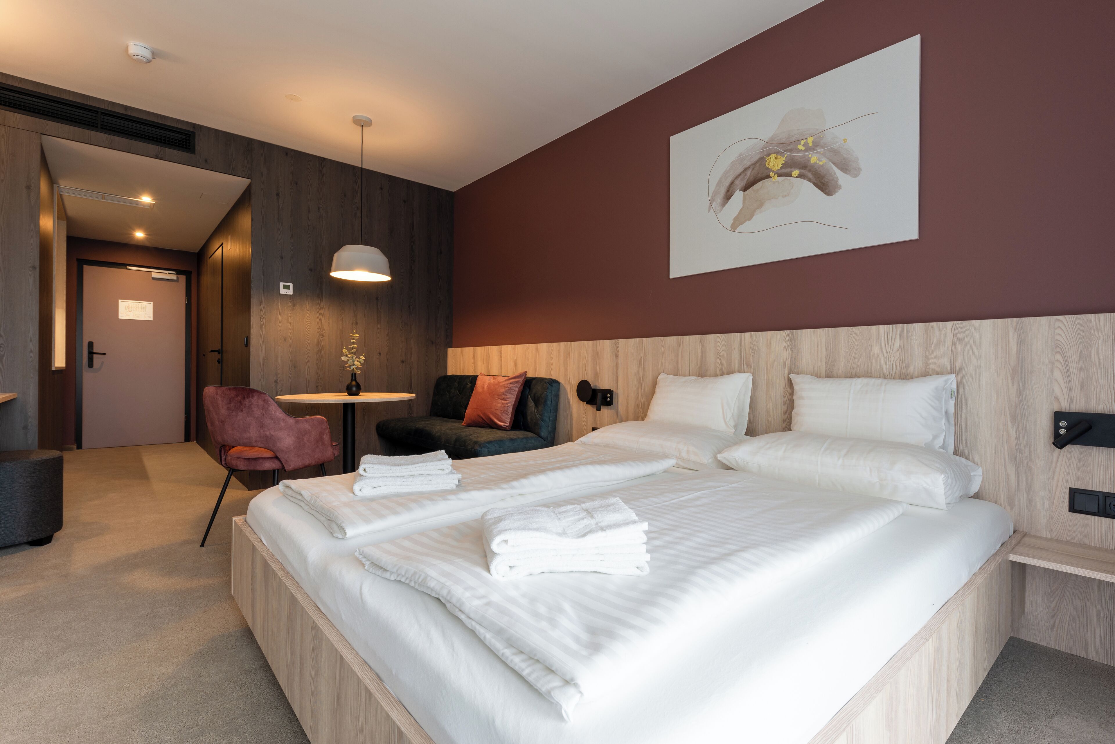 Ein modernes Hotelzimmer mit einem großen Bett, einem kleinen Schreibtisch, einem Stuhl und einer Wandlampe.