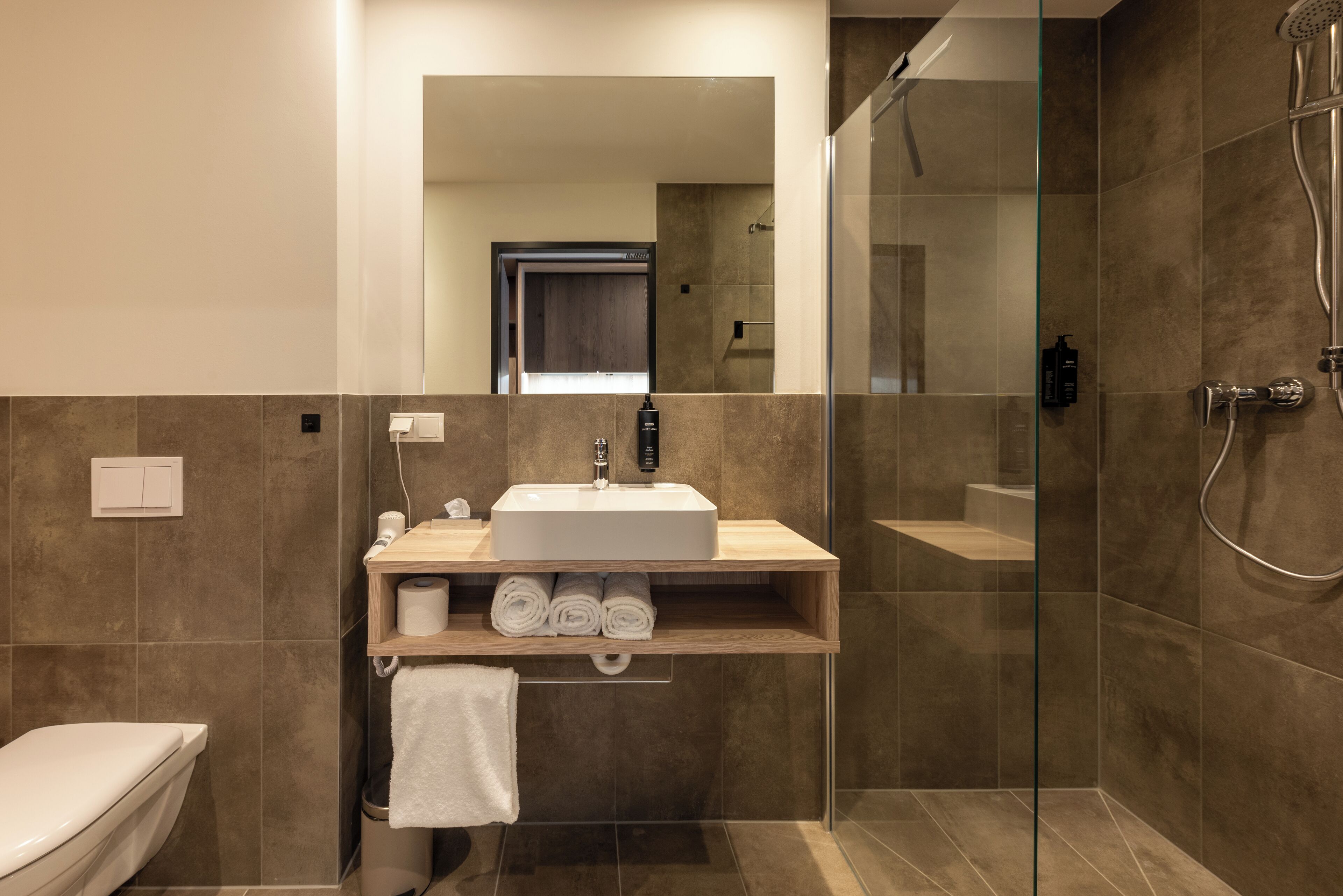 A modern bathroom with a sink, mirror, toilet, and glass-enclosed shower.