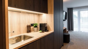 A modern kitchen with a stainless steel sink, wooden cabinets, a built-in oven, and a small countertop area with a plant and a coffee machine. - Hotel Novapart (Wels)