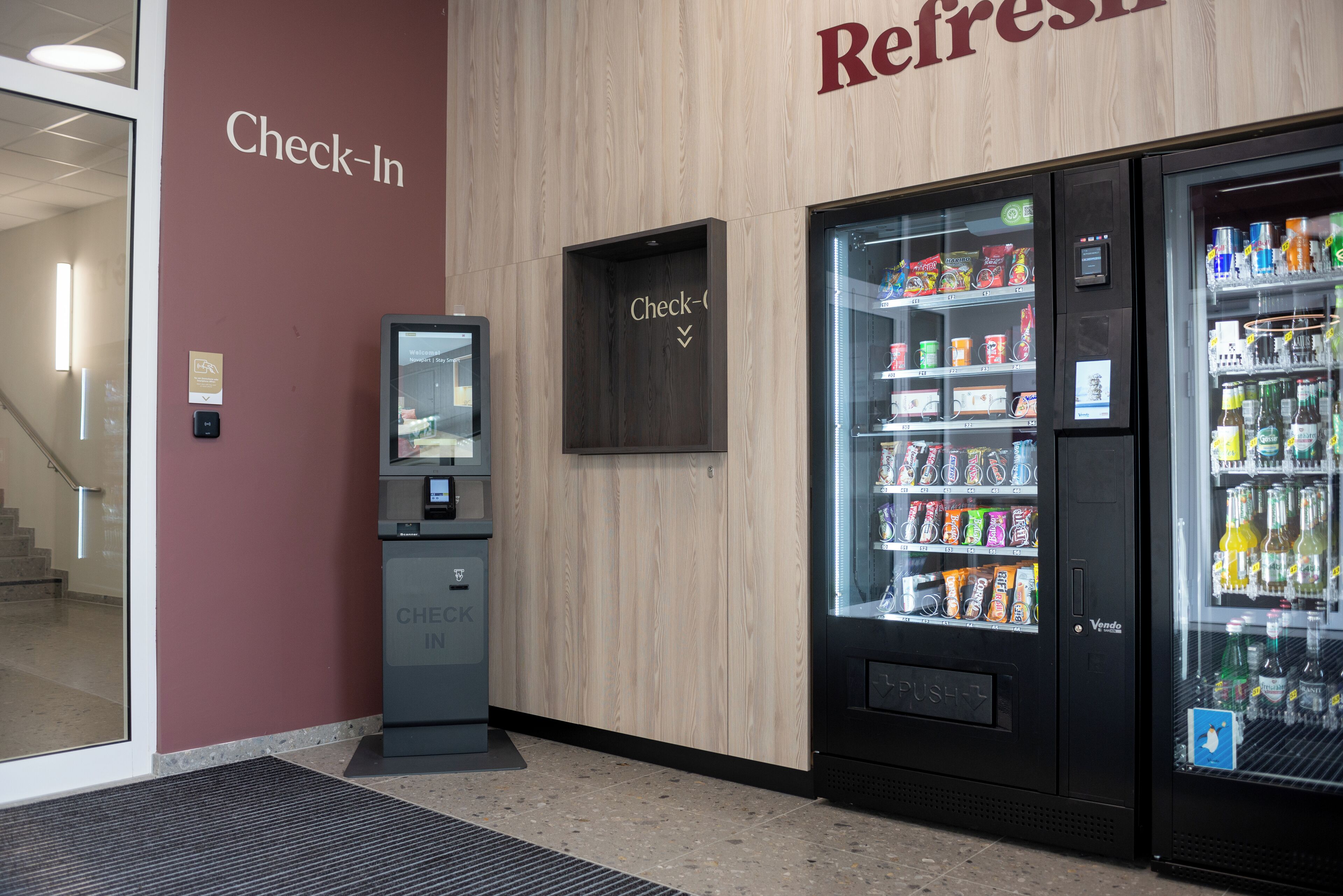 A check-in kiosk and a beverage vending machine in a lobby area.