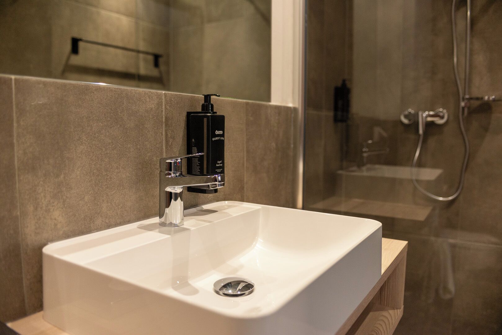 A modern bathroom with a white sink, chrome faucet, and a black soap dispenser.