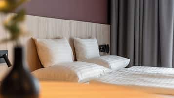 A hotel room with a wooden headboard, two beds with white bedding, a bedside table, and a vase with flowers.
