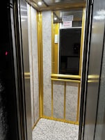 An elevator interior with a metallic finish, a control panel with a digital display, and a sign indicating a maximum weight limit.