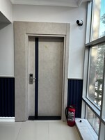 Una puerta con una placa de identificación, un extintor y una ventana que da a vista de árboles.