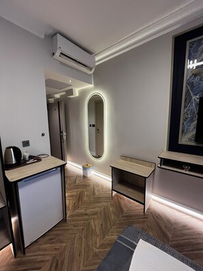 A modern hotel room with a herringbone wood floor, a small kitchenette, a mirror with integrated lighting, and a large framed artwork on the wall. - Hotel Bulut (Erzincan)