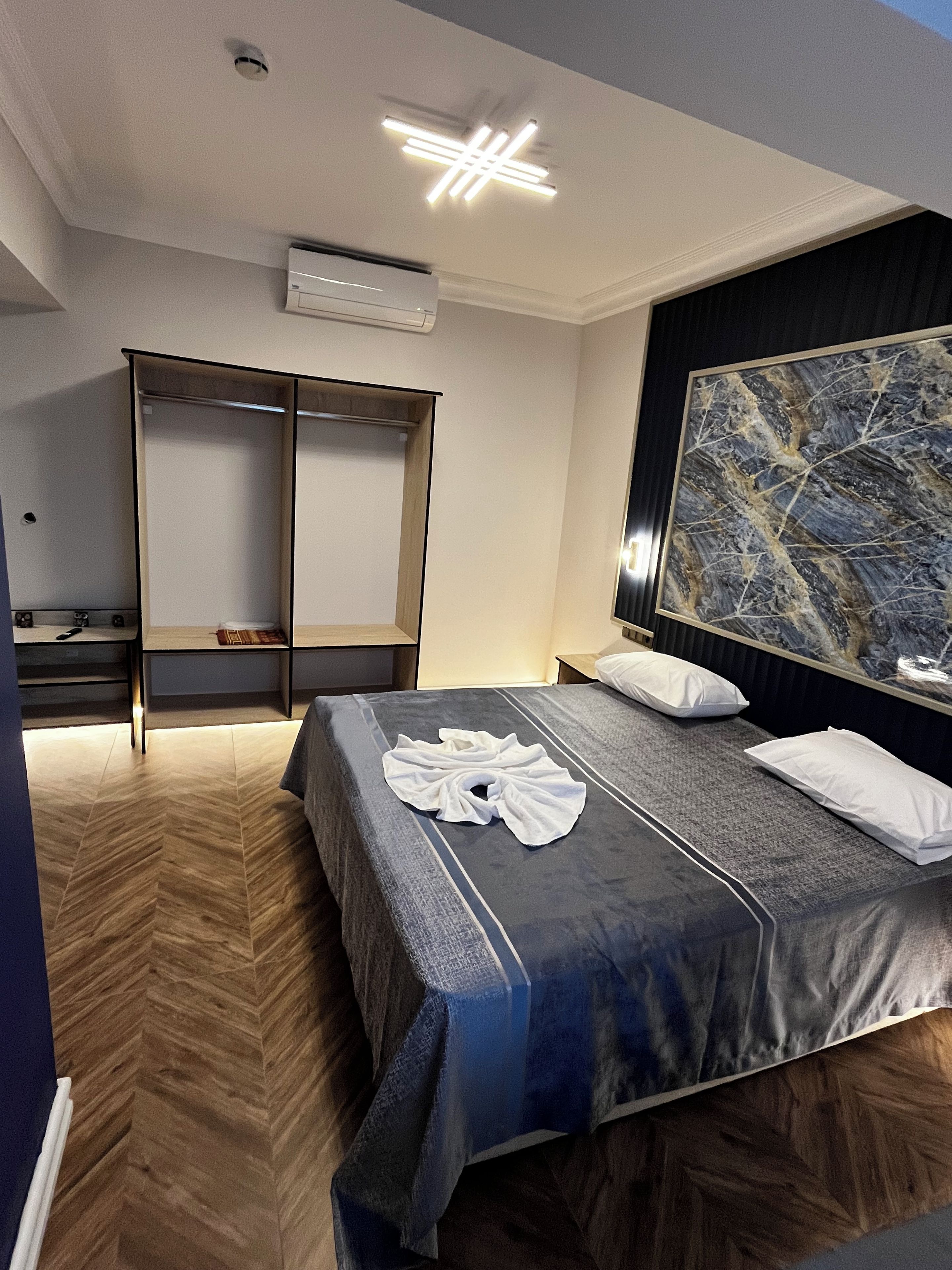 Quarto de hotel com cama, guarda-roupa, mesa de cabeceira e uma grande pintura abstrata na parede.