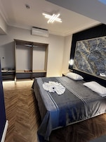 A hotel room with a bed, a wardrobe, a nightstand, and a large abstract painting on the wall.