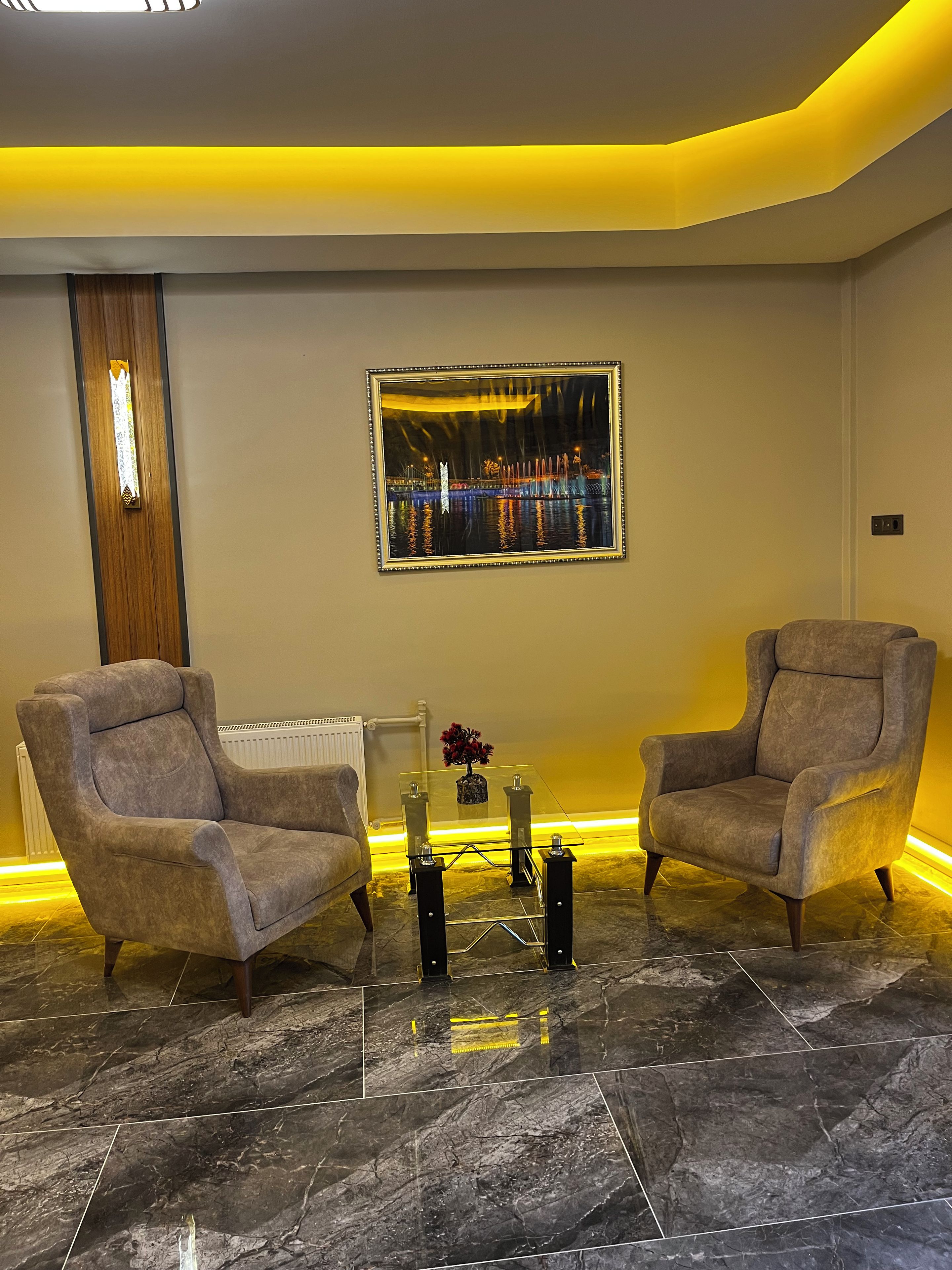 Un salón moderno con dos sillones, una mesa de centro de vidrio y un cuadro con una vista urbana.