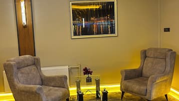 Un salón moderno con dos sillones, una mesa de centro de vidrio y un cuadro con una vista urbana.