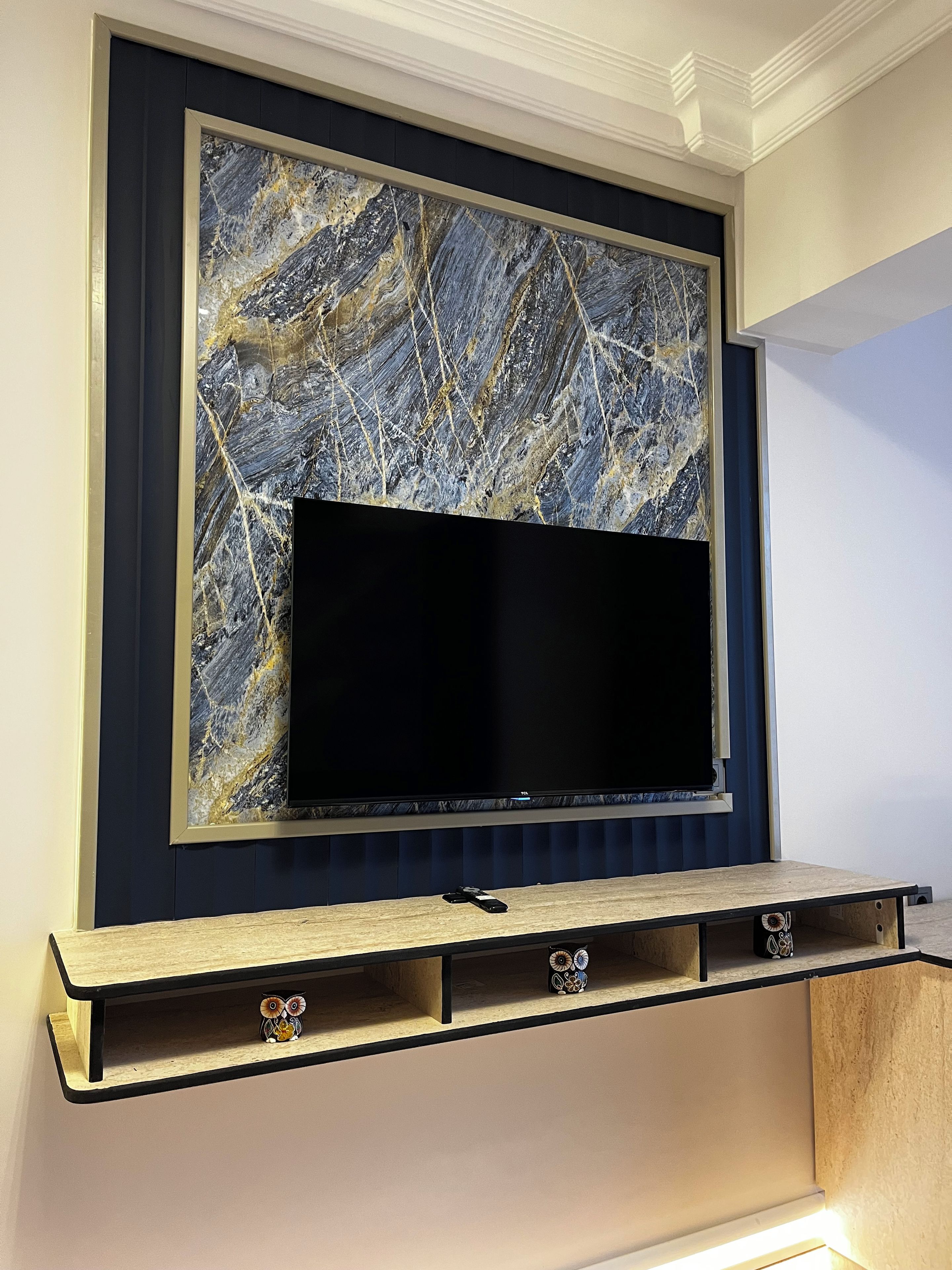 Televisão de tela plana fixada em parede com painel decorativo que imita mármore.