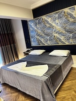 A hotel room with a large bed, a nightstand, a lamp, and a painting on the wall.