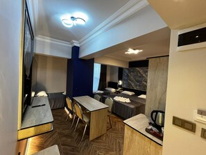 A modern hotel room with a dining area, a bed with a headboard, a large mirror, and a coffee machine. - Hotel Bulut (Erzincan)