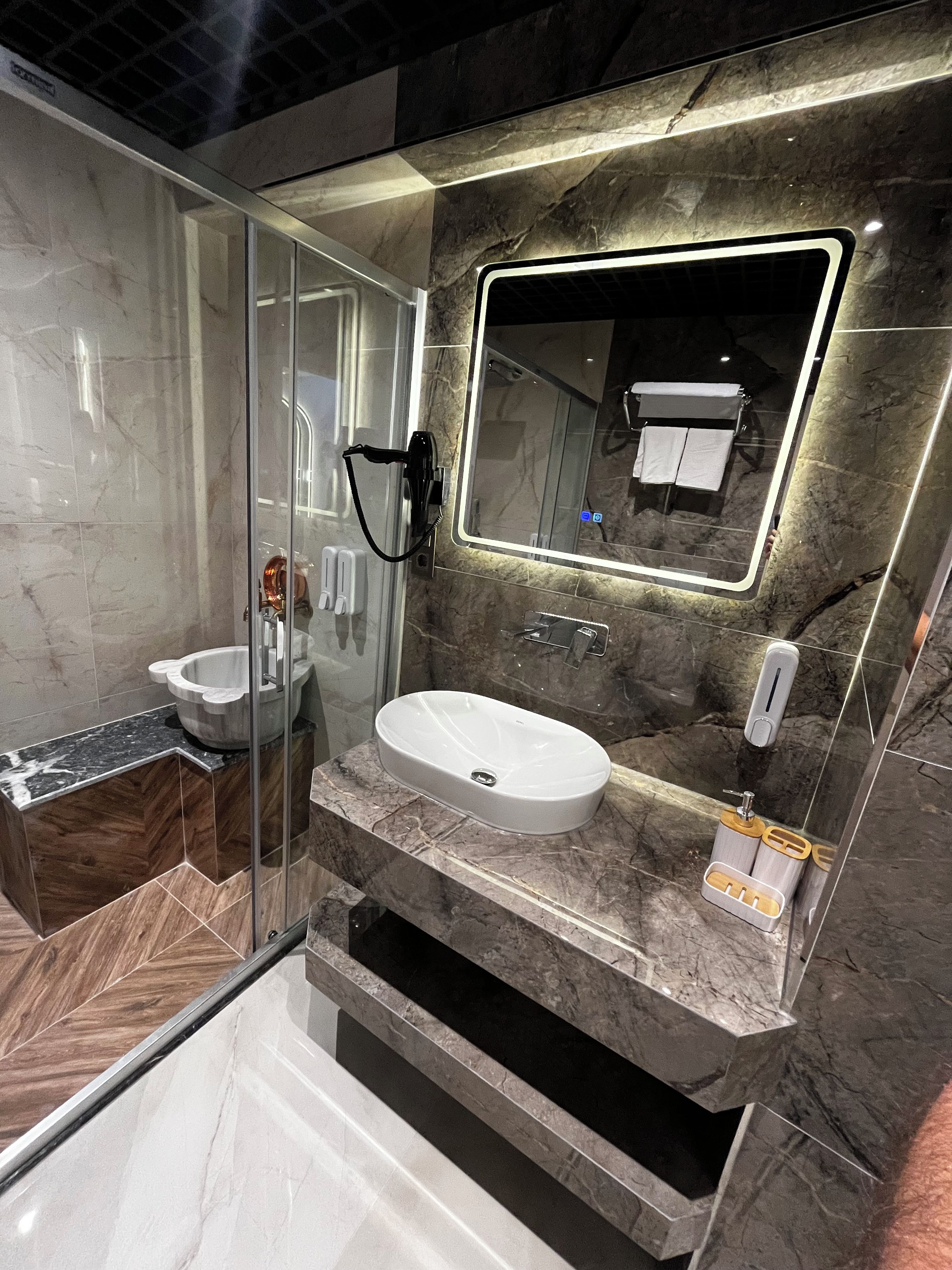 A modern bathroom with a glass-enclosed shower, a marble sink, and a large mirror.