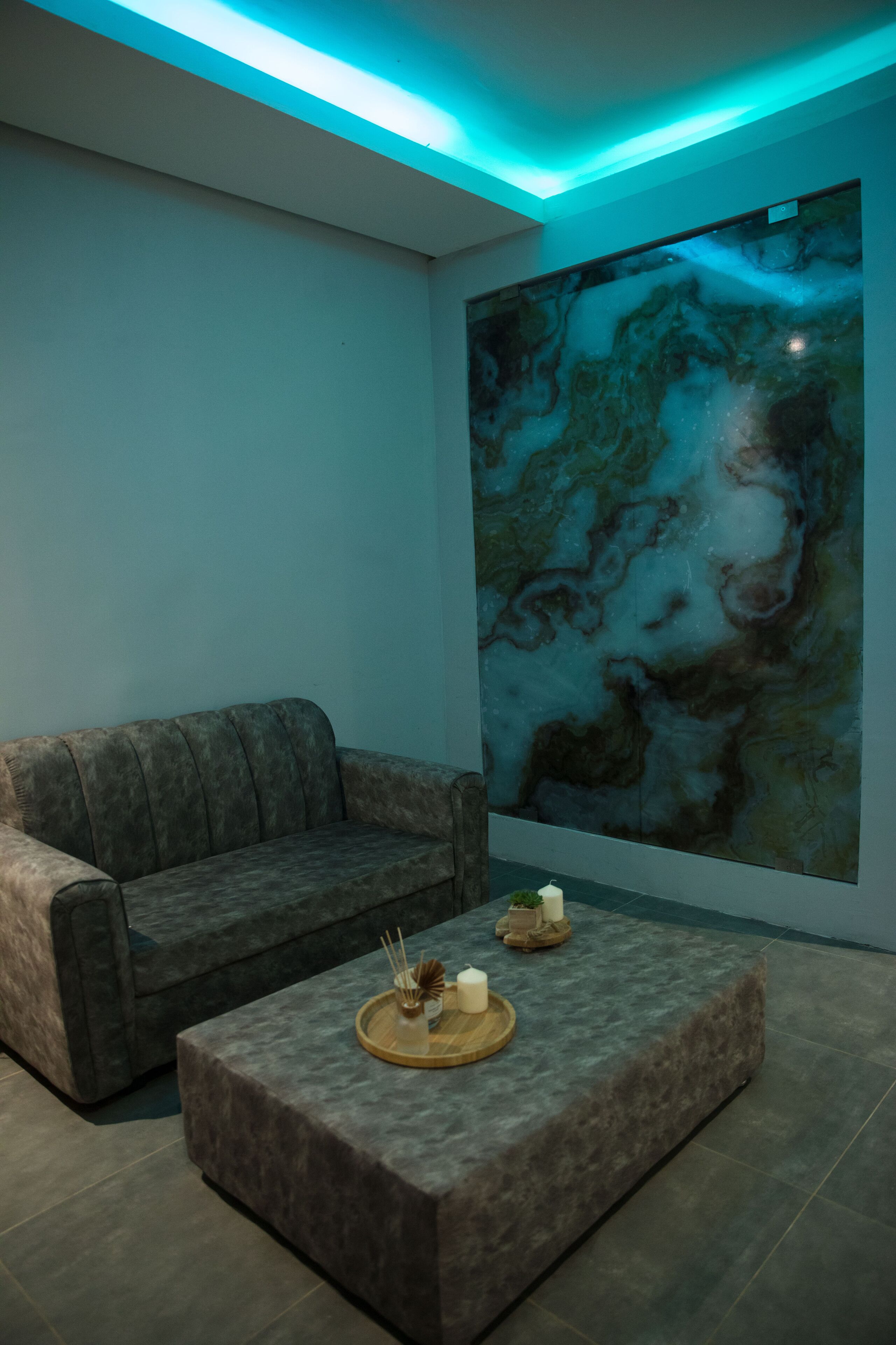 A modern living room with a grey sofa, a small ottoman with candles, and a large abstract painting on the wall.