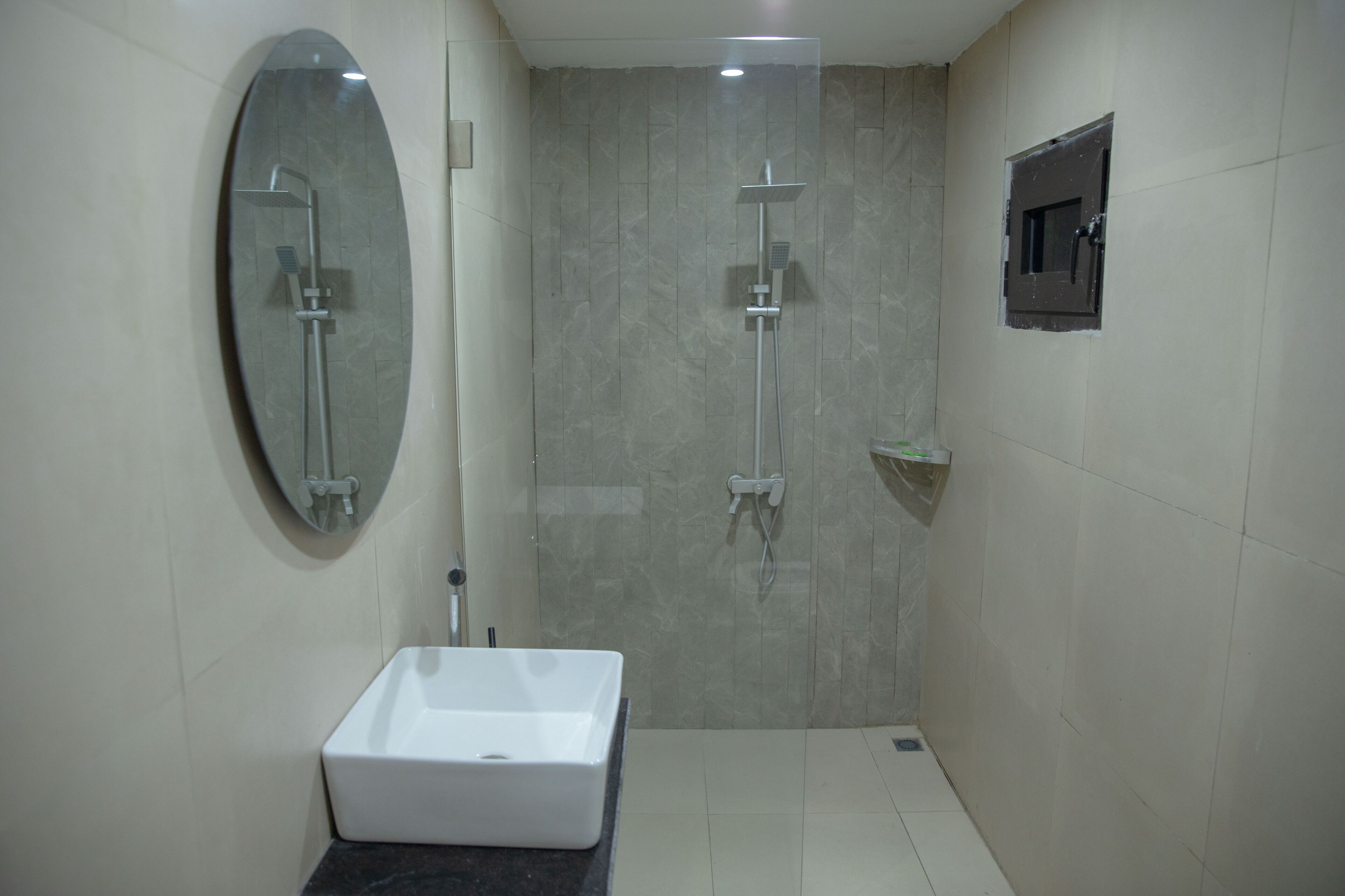 Une salle de bain moderne avec un lavabo rectangulaire, un grand miroir ovale et un espace douche doté d’une porte en verre.
