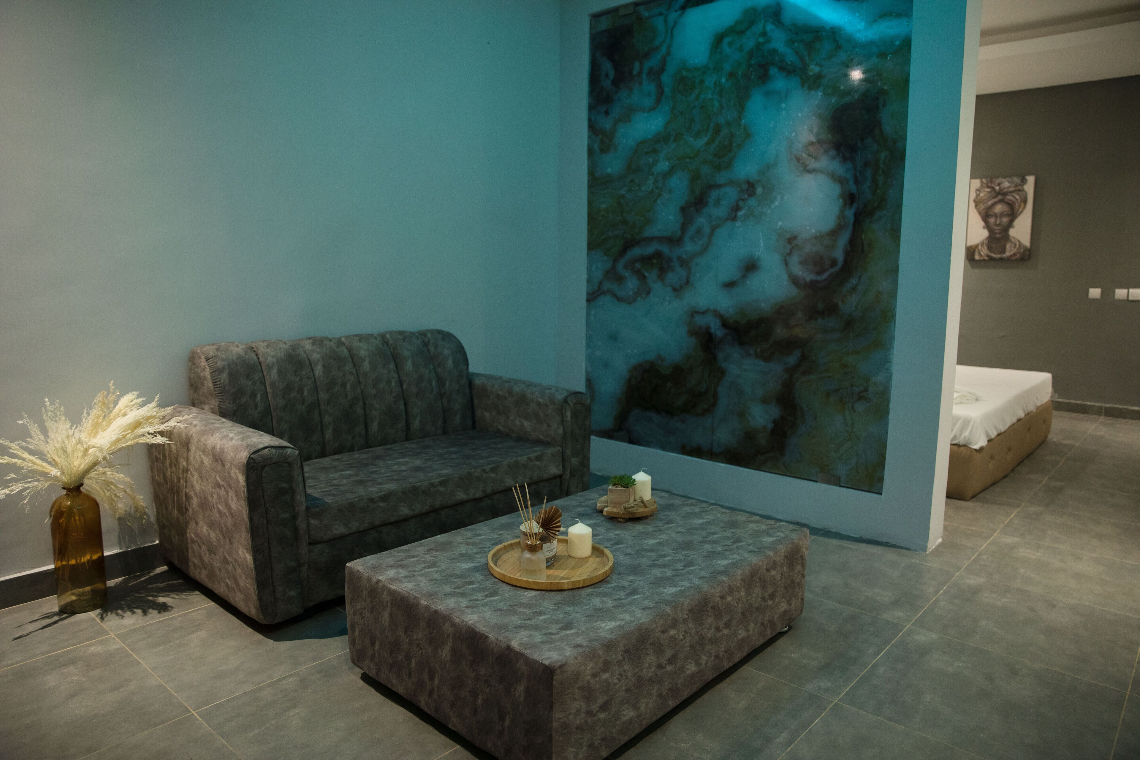 Une pièce moderne avec un canapé gris, un petit pouf muni d’un plateau, et un grand tableau abstrait accroché au mur.