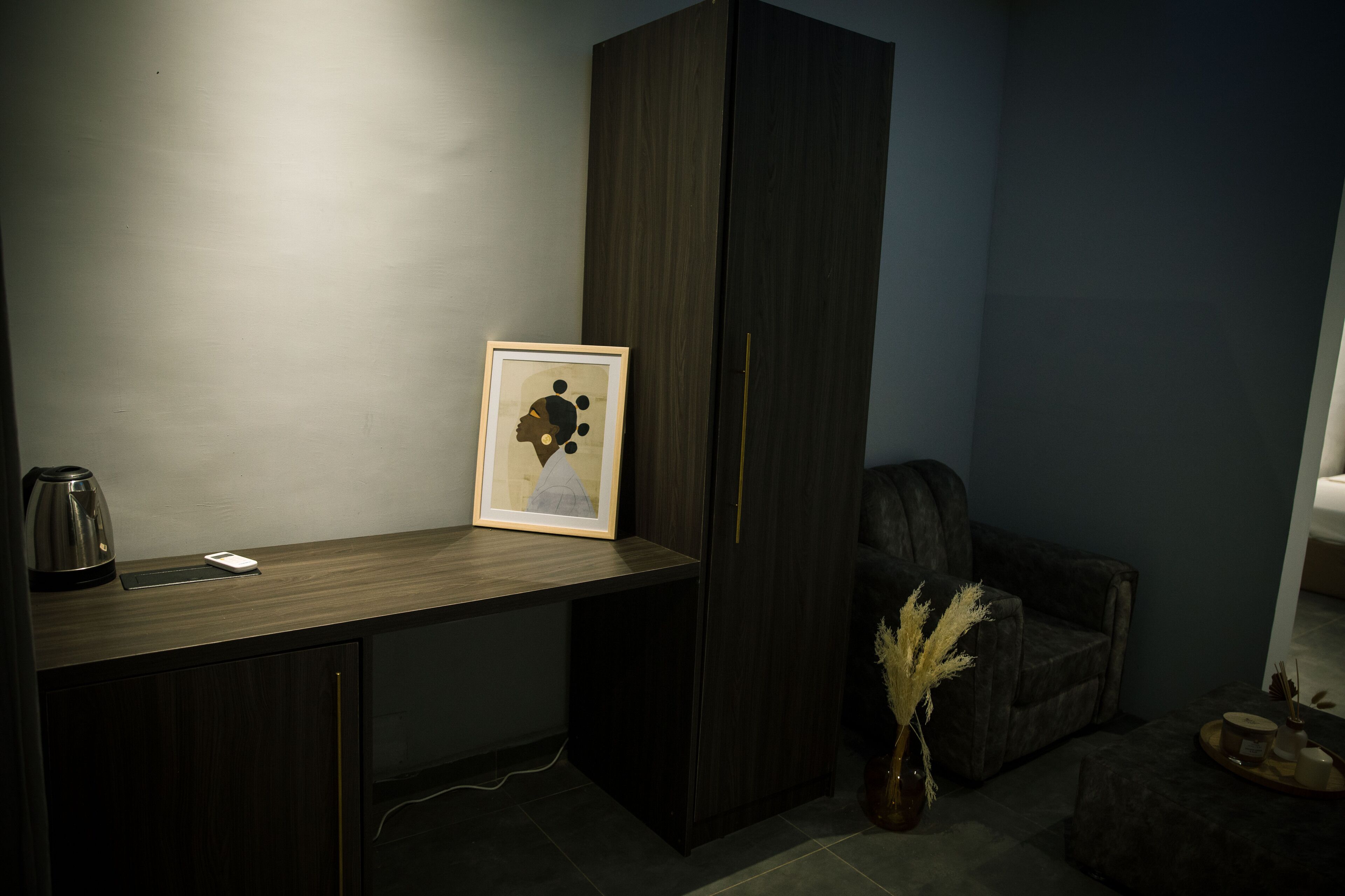 Un bureau en bois foncé, orné d’un tableau encadré, avec une machine à café et un vase contenant des plantes séchées.