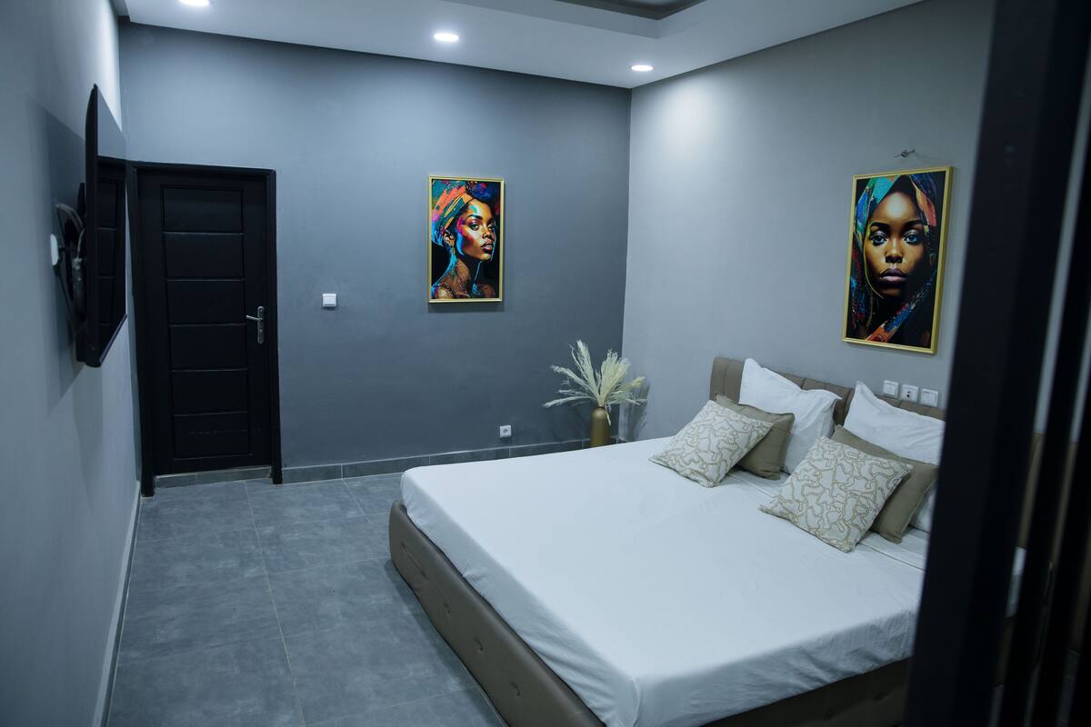 A bedroom with a bed, a door, and two framed artworks on the wall.