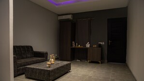 A modern living room with a grey sofa, a matching ottoman, and a dark wooden cabinet. - The SHELTER (Abidjan)