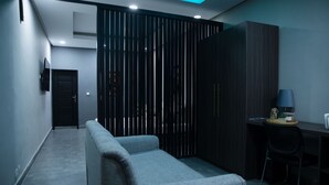 A modern room with a grey sofa, a desk with a lamp, and a wardrobe. - The SHELTER (Abidjan)