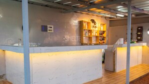 A bar area with a marble countertop, shelves with bottles, and a wooden bar stool. - The SHELTER (Abidjan)