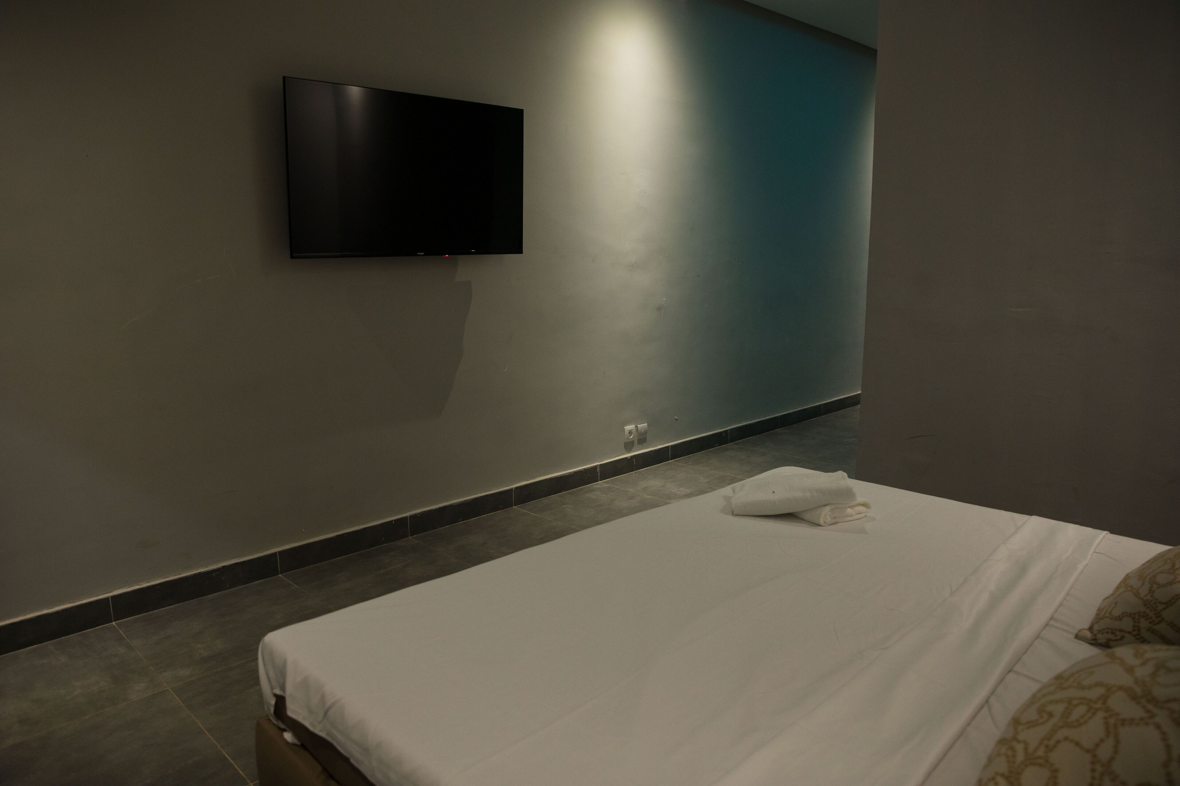 Una habitación de hotel con una cama, un televisor de pantalla plana montado en la pared y una toalla sobre la cama.