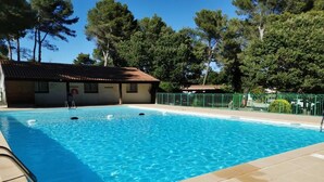 Ein Schwimmbecken mit klarem, blauem Wasser, umgeben von einer gefliesten Terrasse und einem grünen Zaun.