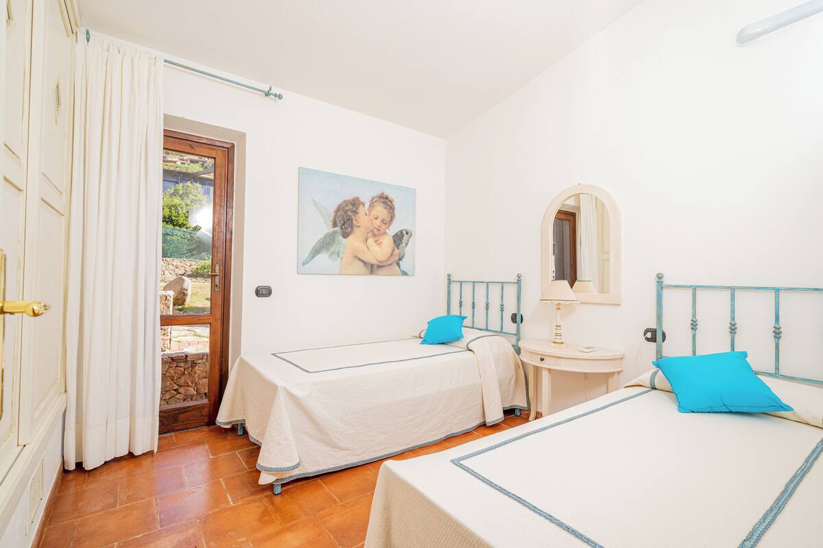 A bedroom with two beds, a small bedside table, a mirror, and a door leading to an outdoor area.