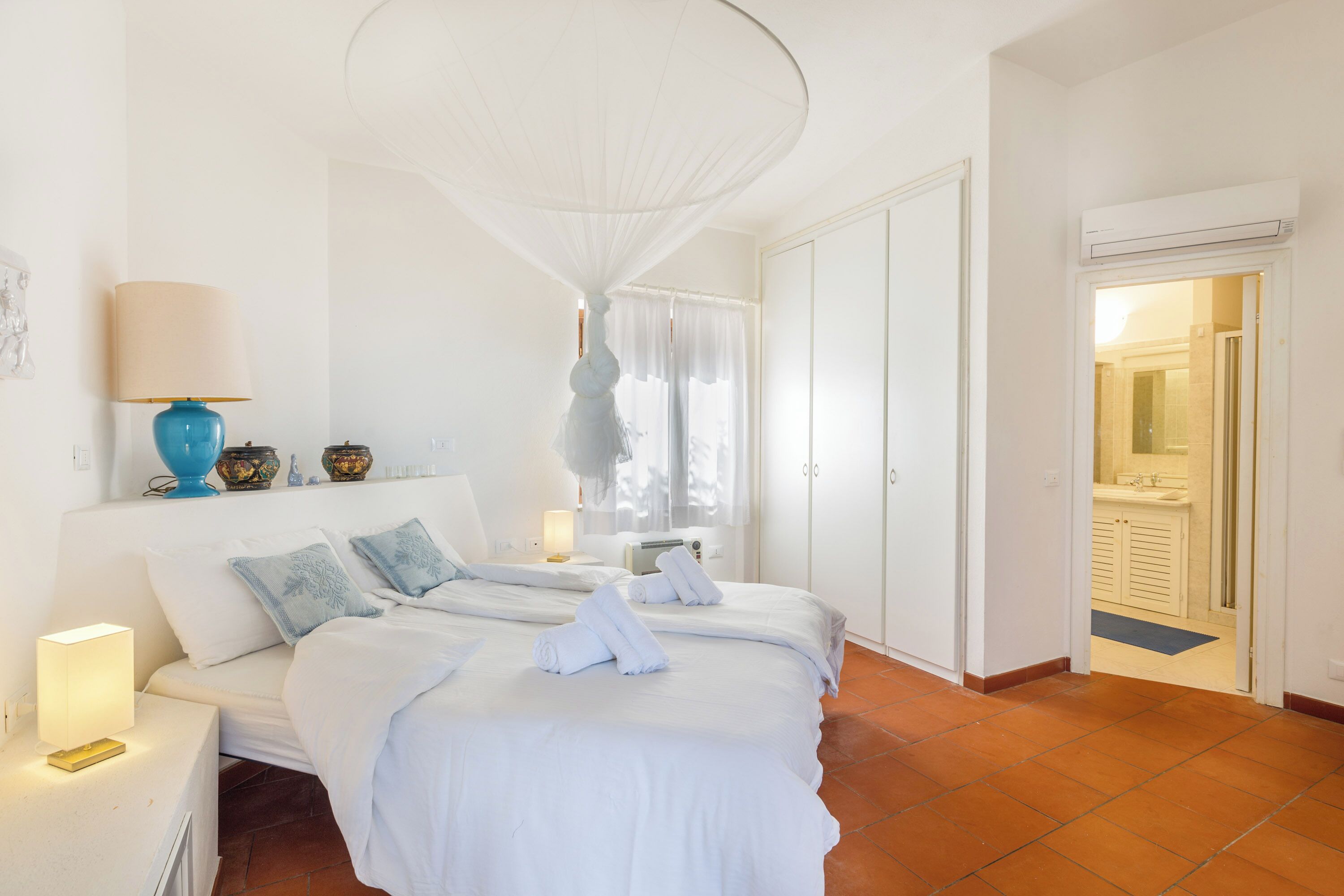 Une chambre d’hôtel avec un grand lit, des tables de chevet, une lampe, un ventilateur de plafond et une vue sur la salle de bain.
