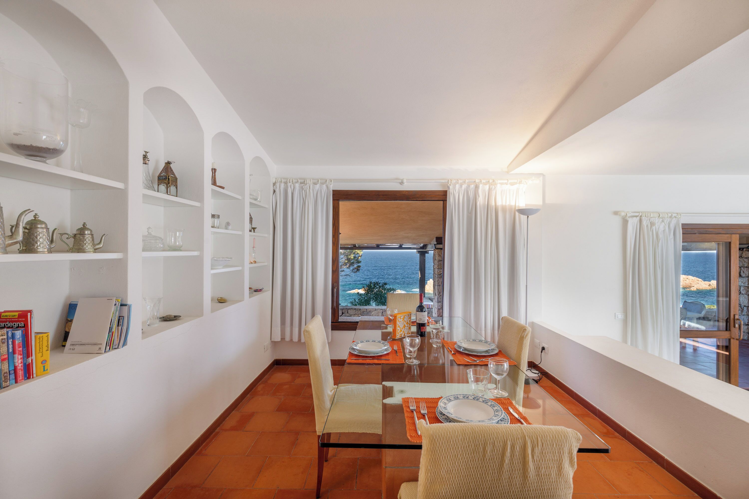 Un coin repas avec une table dressée pour quatre personnes, des murs blancs et une vue sur la mer.