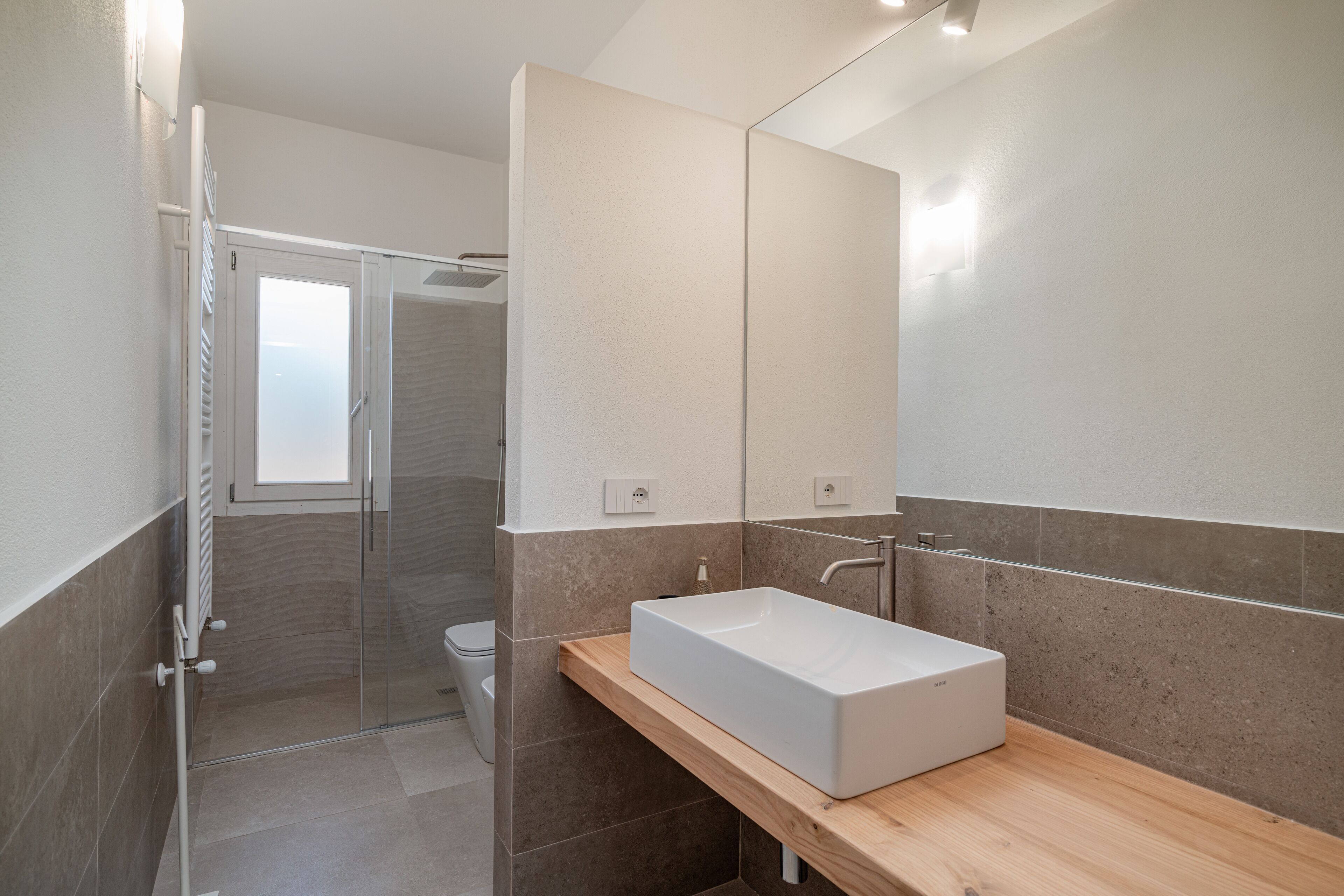 Une salle de bain moderne avec un grand miroir, un lavabo rectangulaire et un espace douche.