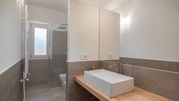 Une salle de bain moderne avec un grand miroir, un lavabo rectangulaire et un espace douche.