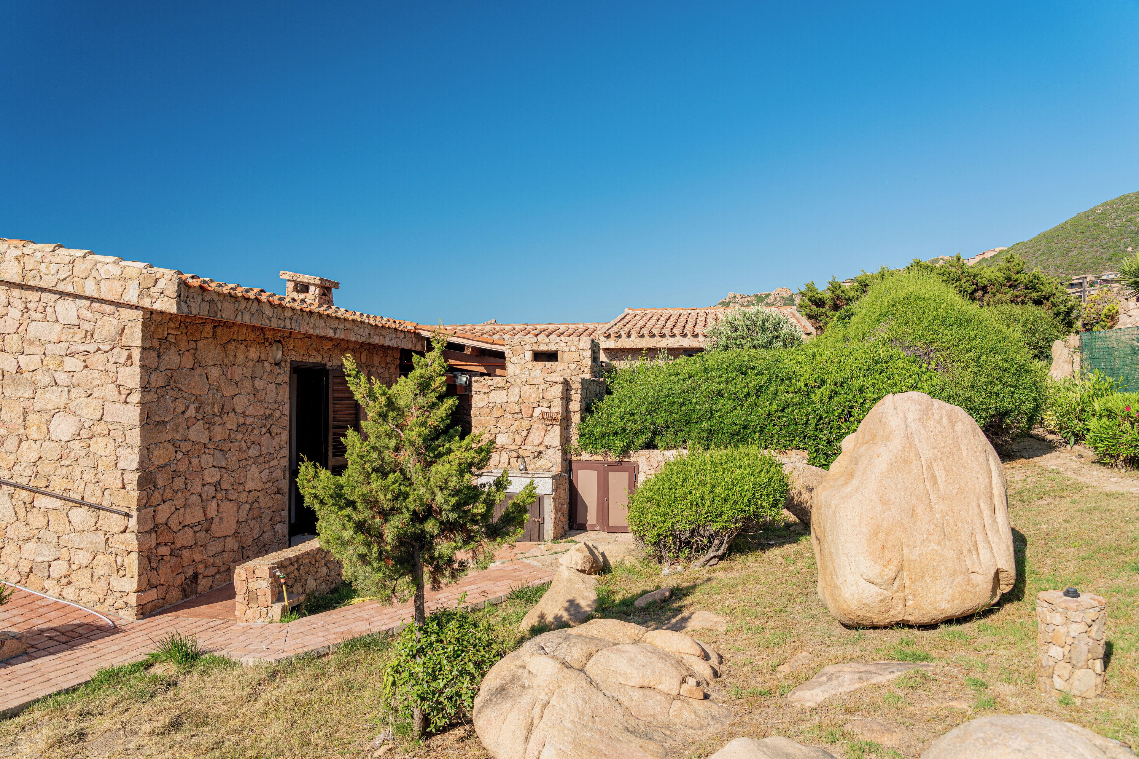 A stone building with a tiled roof, surrounded by rocks and greenery.