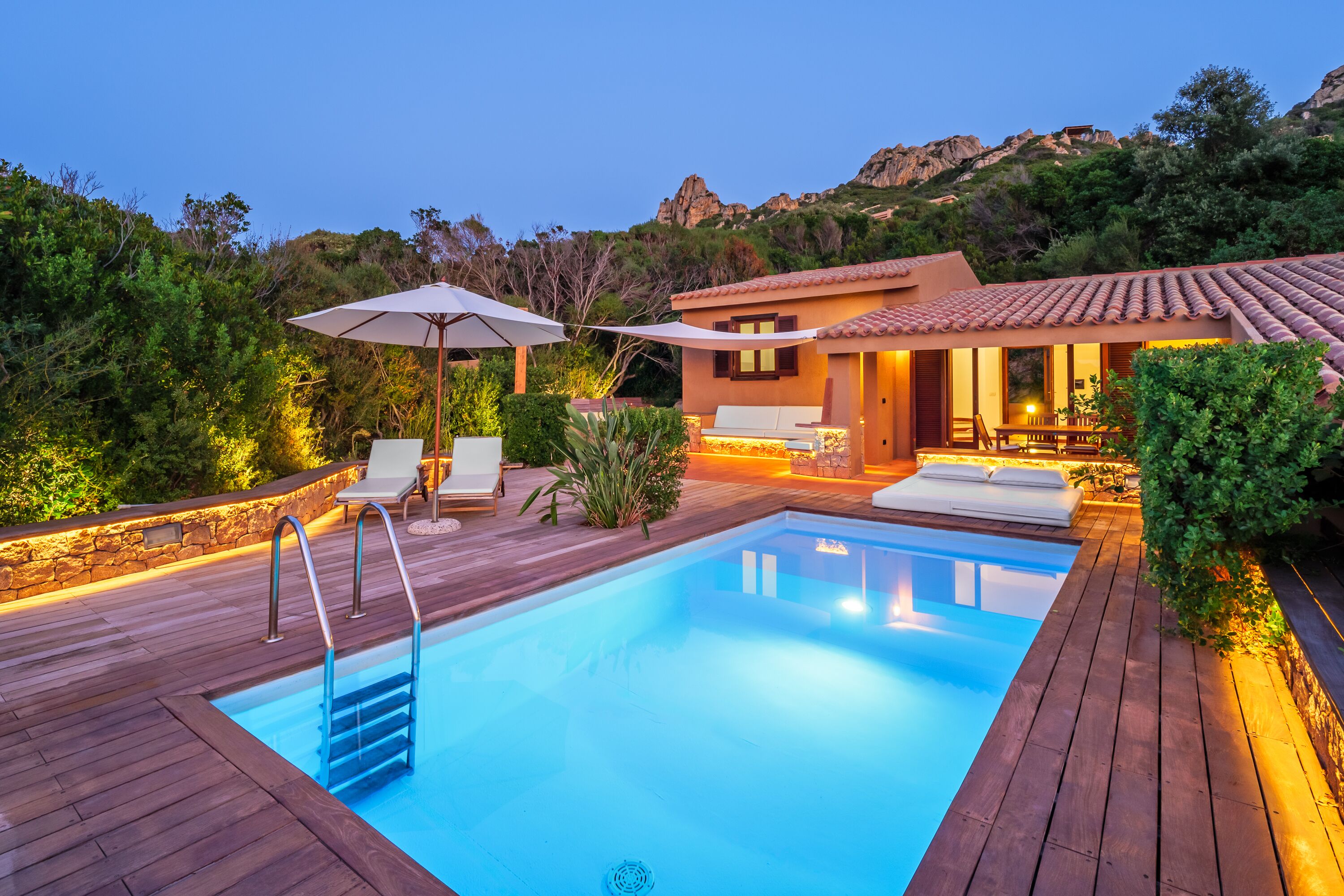 Une piscine entourée d’une terrasse en bois, de chaises longues et d’un espace extérieur aménagé avec une table et des chaises.