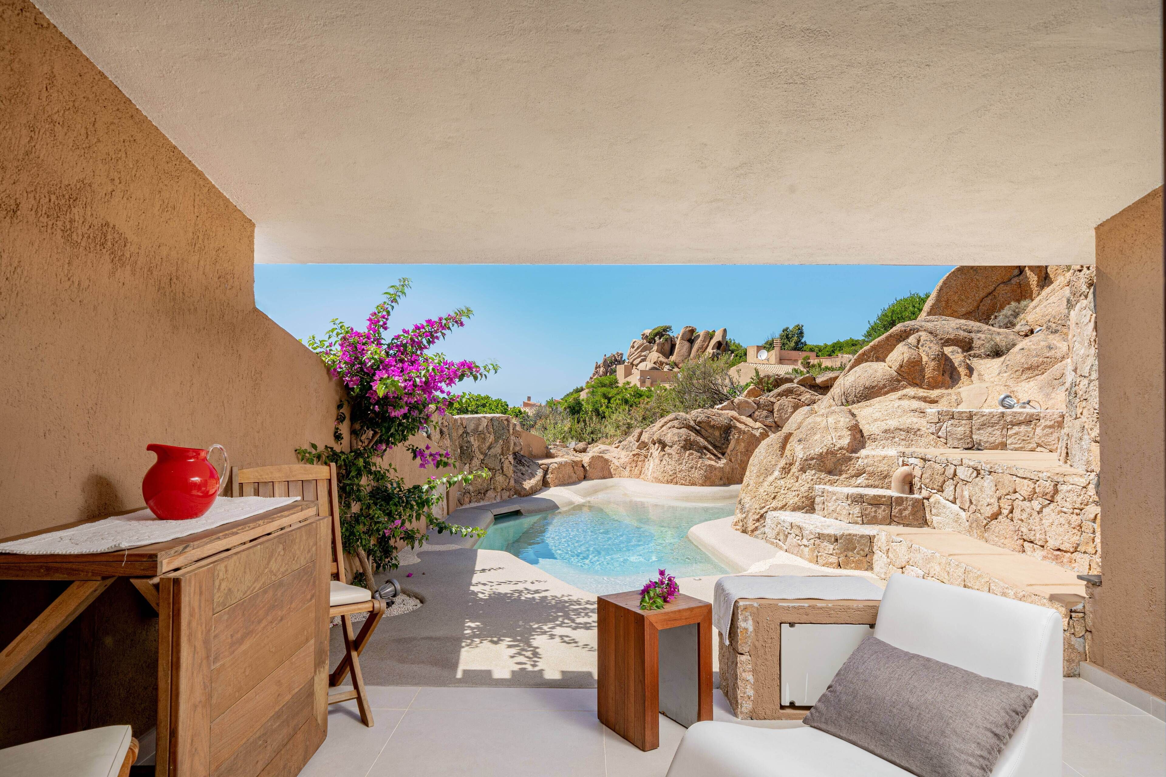 A sunlit outdoor seating area with a pool, stone steps, and a view of rocky terrain.