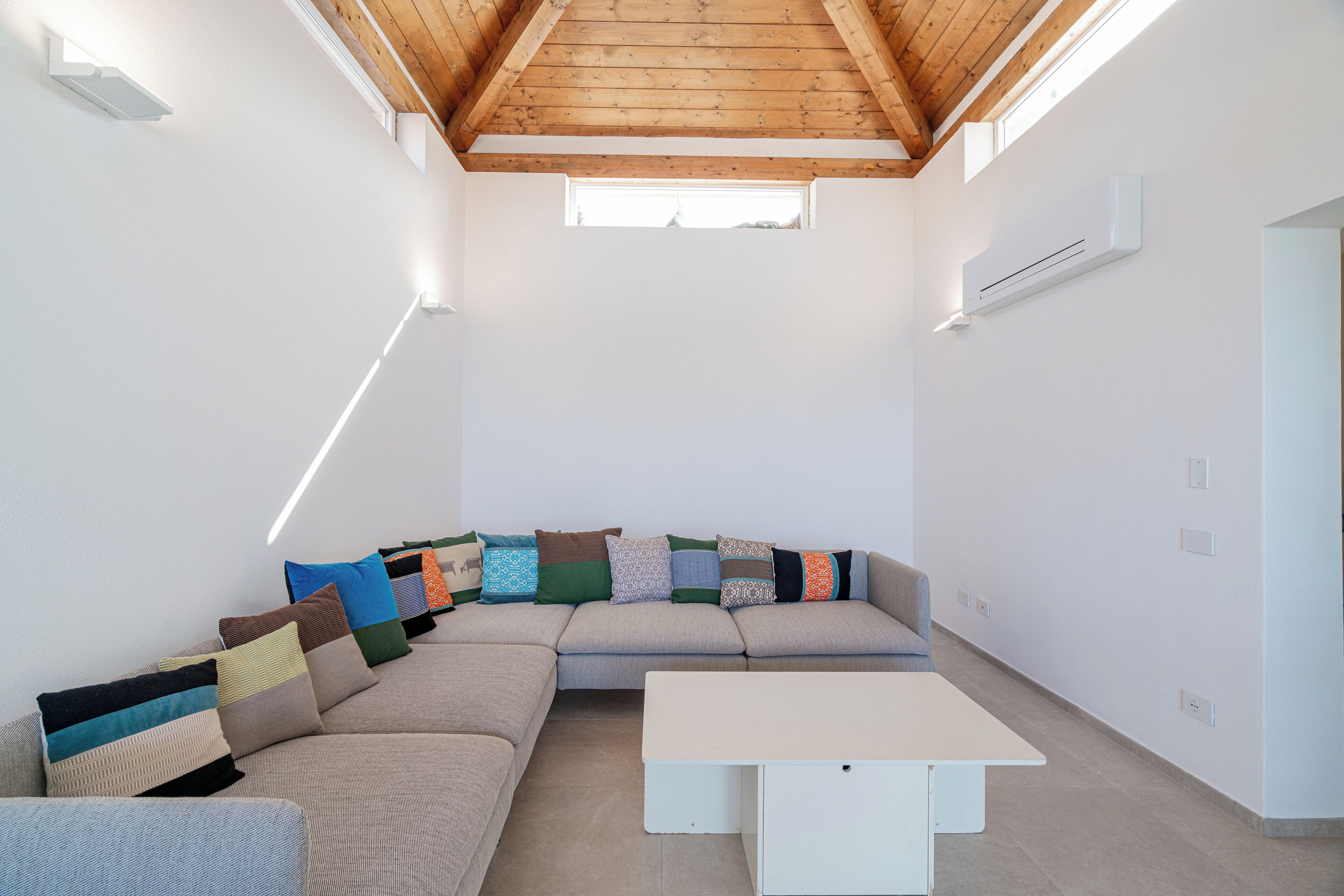A modern living room with a sectional sofa, a white table, and a sloped wooden ceiling with skylights.