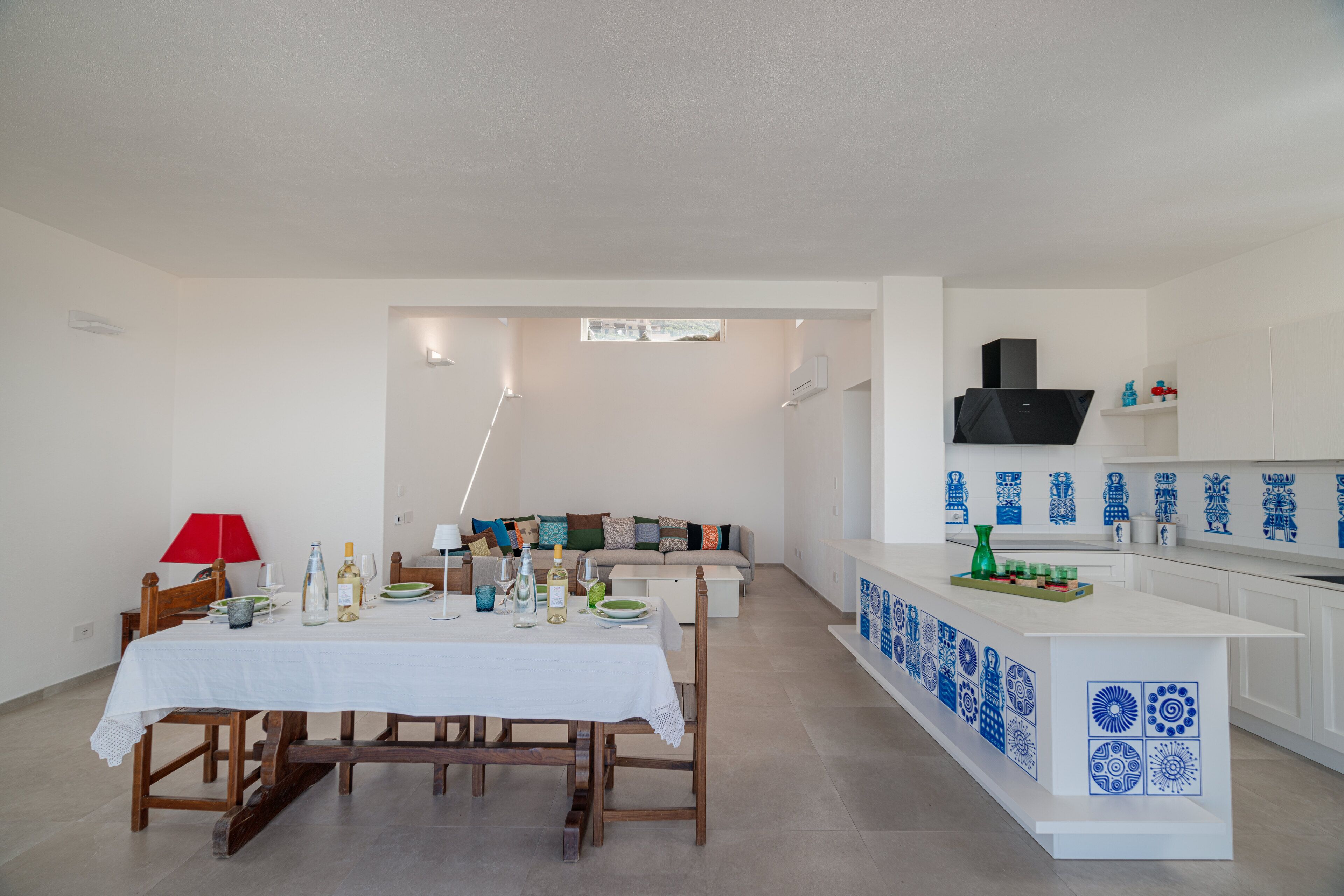 A modern kitchen with white cabinets, blue decorative tiles, and a dining area with a white table and chairs.