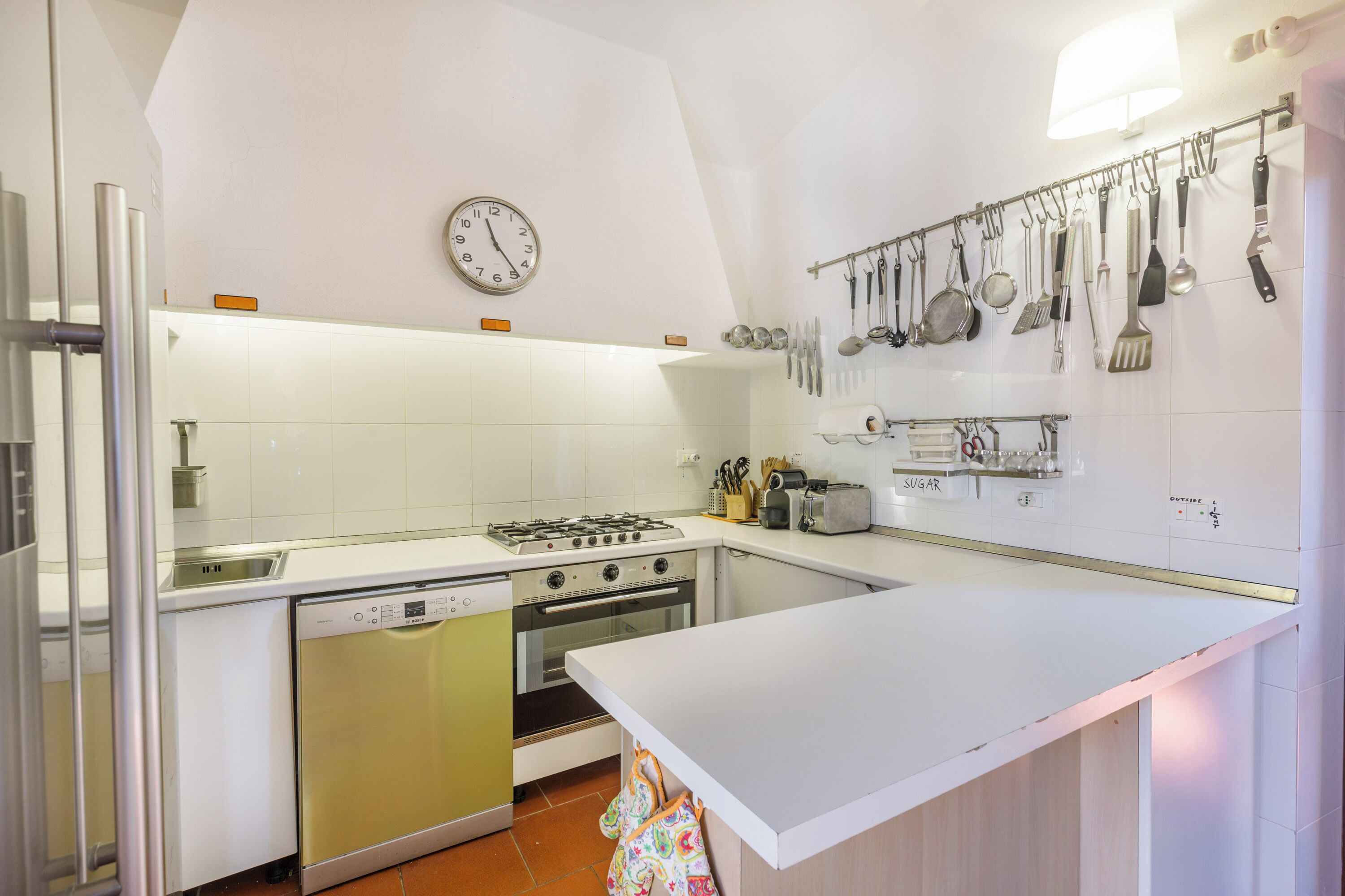 A compact kitchen with white cabinets, a gas stove, a dishwasher, and a wall-mounted utensil rack.